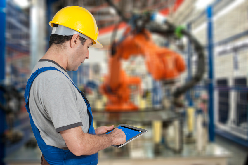 Factory worker using tablet to operate a robotic arm