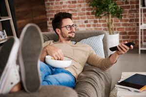 man on couch watching tv eating popcorn