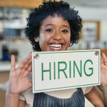 Portrait of a young woman holding a "hiring" sign in her store