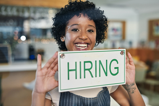 Portrait of a young woman holding a "hiring" sign in her store