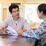 Woman in uniform sits at a table with a man as they look through papers